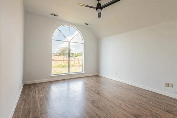 an empty room with wooden floor fan and windows