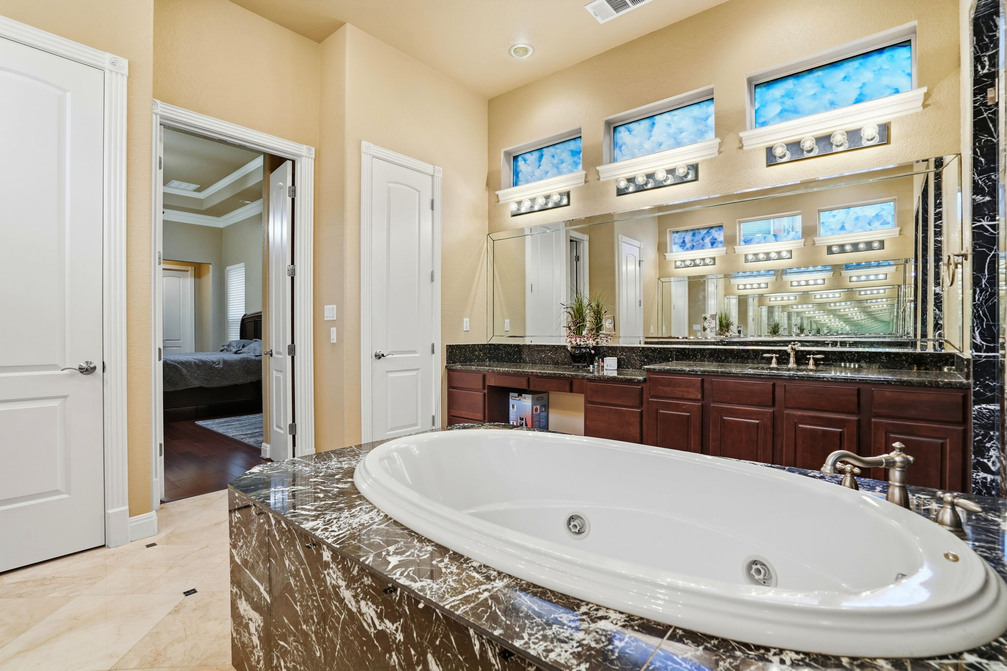 222 Vailco Lane Austin, TX 78738 - Photo 35 of 39 Soaking tub with a dark marble surround, dual vanities with dark wood cabinetry, a large wall-mounted mirror, and decorative transom windows with custom lighting fixtures