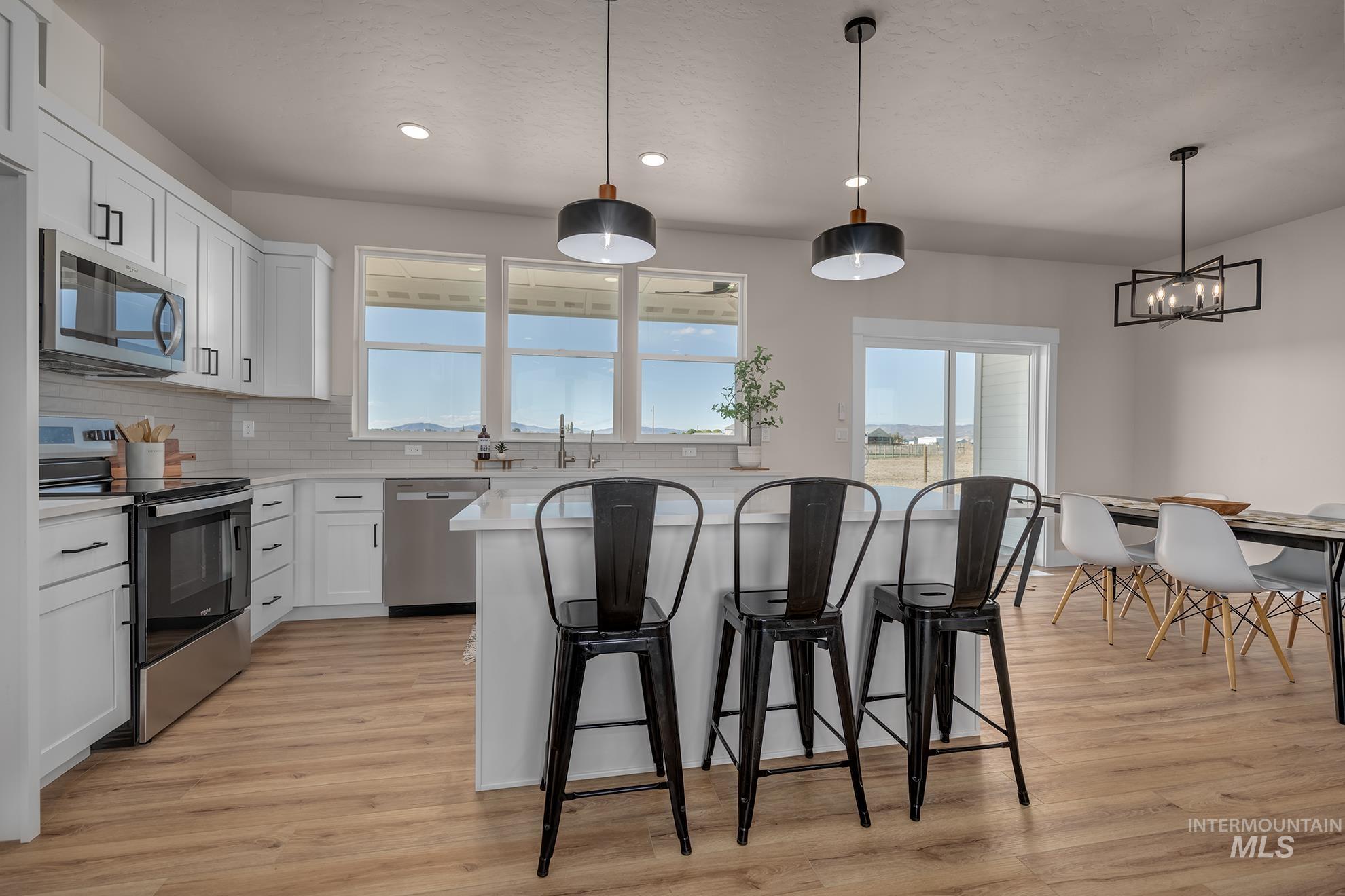 1371 Hansen Road Weiser, ID 83672 - Photo 12 of 44 Modern kitchen featuring white shaker cabinetry, stainless steel appliances, wood-finish flooring, a kitchen island with seating, and a dining area with contemporary lighting