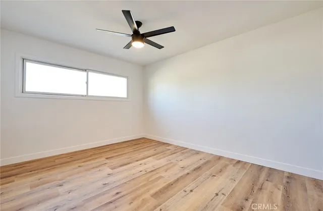 an empty room with wooden floor fan and windows