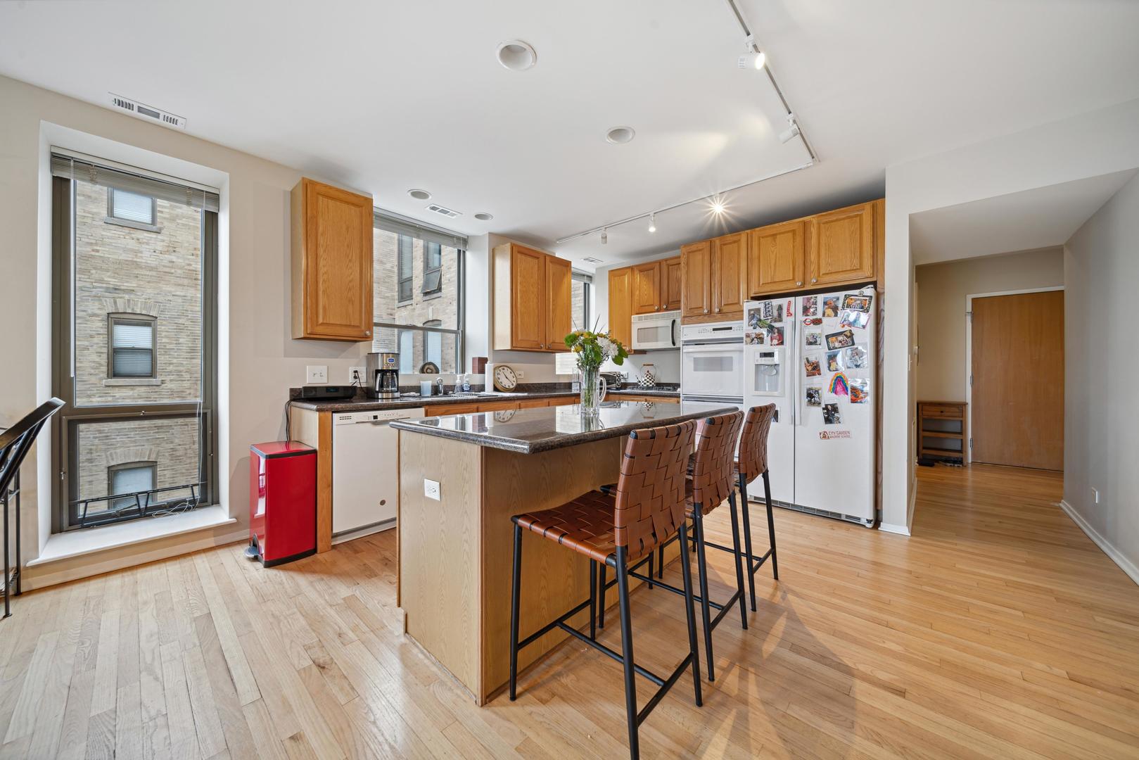 811 South Lytle Street, Unit 510 Chicago, IL 60607 - Photo 11 of 26 a kitchen with stainless steel appliances kitchen island granite countertop a refrigerator a stove top oven and a dining table with wooden floor
