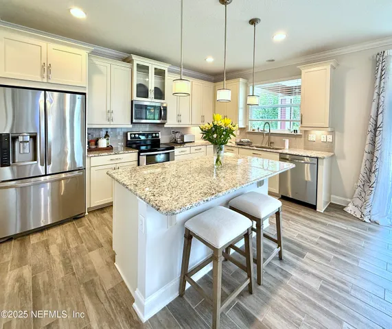 a kitchen with stainless steel appliances granite countertop a refrigerator a stove top oven a sink dishwasher a dining table and chairs with wooden floor