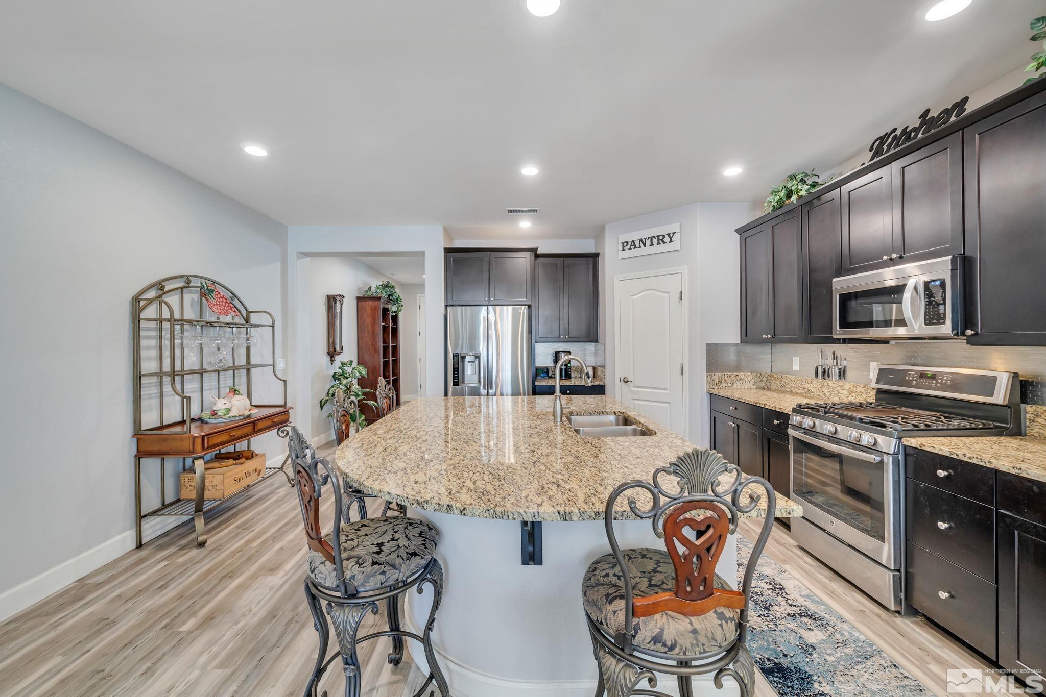 10128 Quintana Drive Reno, NV 89521 - Photo 8 of 34 a kitchen with stainless steel appliances granite countertop a stove top oven a sink a dining table and chairs with wooden floor