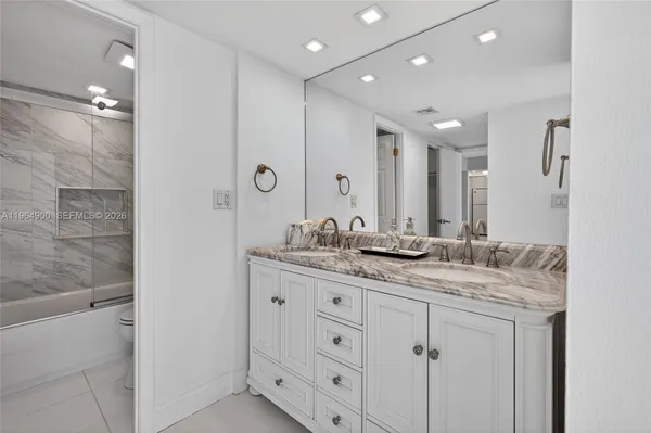 a bathroom with a granite countertop sink two mirror and shower