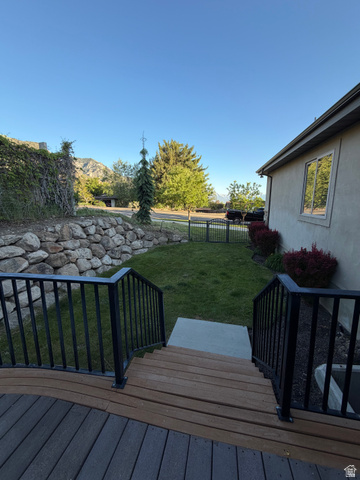 4536 North 475 East Provo, UT 84604 - Photo 56 of 65 Wood-finish deck with black metal railings descending to a manicured lawn, bordered by a rock retaining wall and lush landscaping