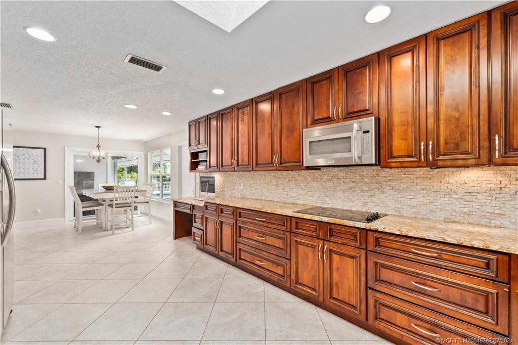 18770 Southeast River Ridge Road Jupiter, FL 33469 - Photo 9 of 81 a kitchen with stainless steel appliances granite countertop wooden cabinets a dining table and chairs