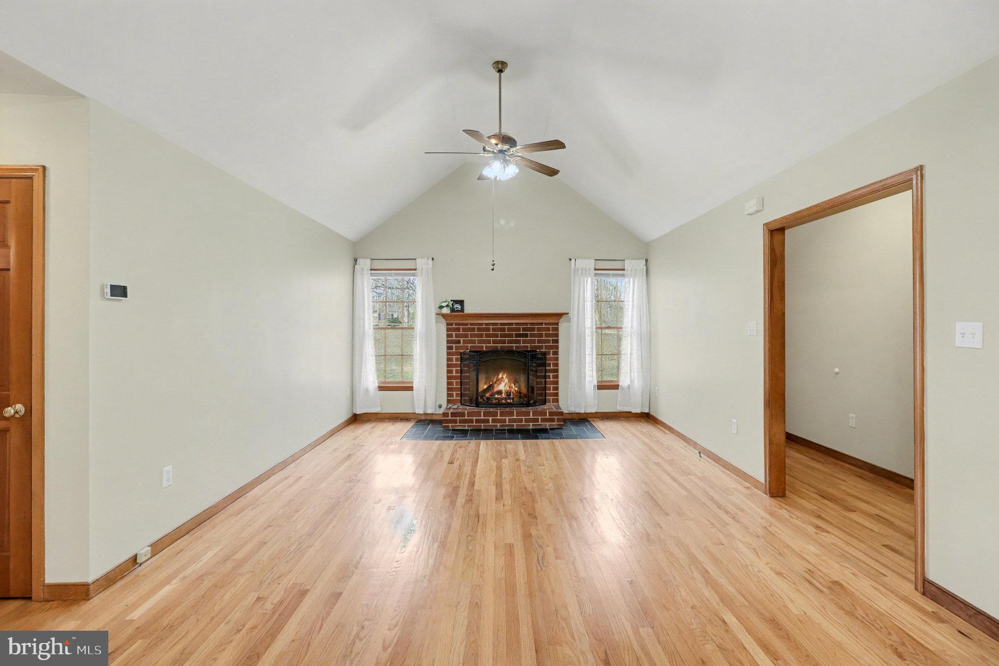 259 Hawkins Farm Road Bumpass, VA 23024 - Photo 4 of 24 an empty room with wooden floor fireplace and a ceiling fan