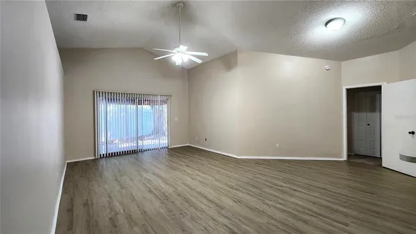 an empty room with wooden floor chandelier fan and windows