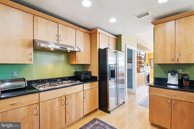 a kitchen with stainless steel appliances granite countertop a refrigerator a stove and white cabinets with wooden floors