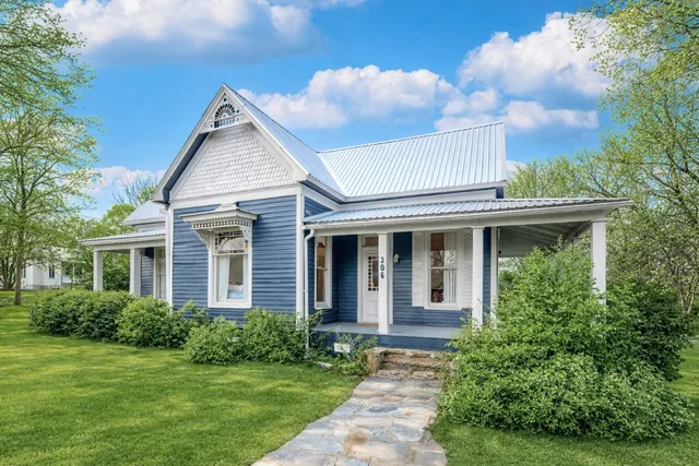a view of a white house next to a yard with plants and trees