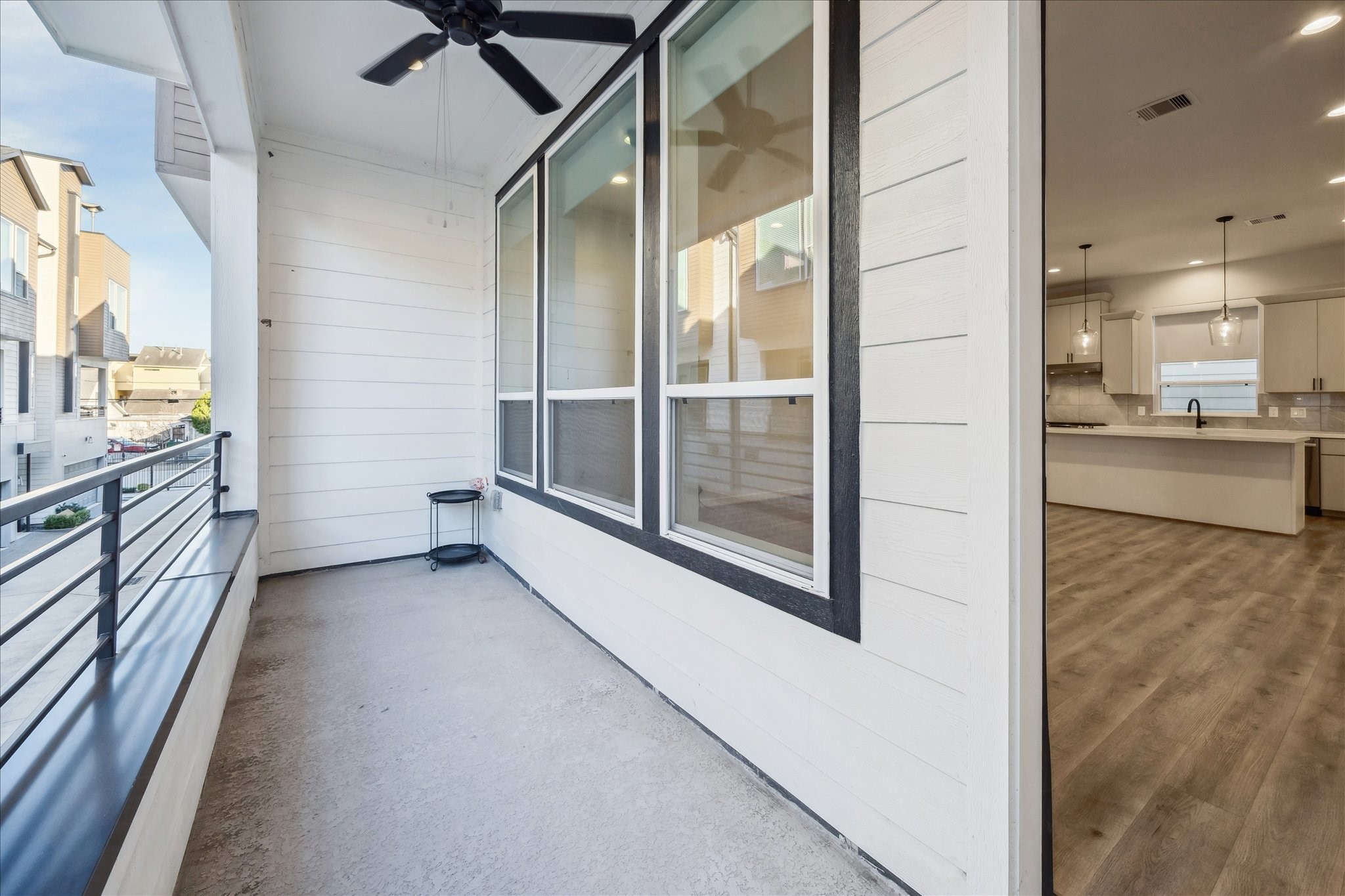1603 Patterson Street, Unit E Houston, TX 77007 - Photo 32 of 32 This photo showcases a modern, covered balcony with a ceiling fan and railing, adjacent to a spacious, open-concept kitchen and living area.