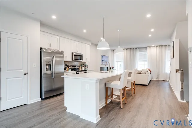 a kitchen with stainless steel appliances kitchen island granite countertop a refrigerator a stove a sink a dining table and chairs with wooden floor