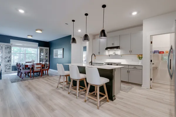 a kitchen with stainless steel appliances kitchen island granite countertop a refrigerator a stove a sink a dining table and chairs with wooden floor