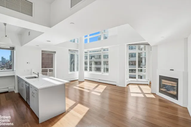 a large white kitchen with granite countertop a stove top oven a sink a refrigerator and white cabinets with wooden floor