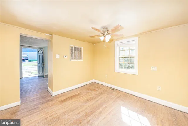 a view of an empty room with wooden floor and a ceiling fan