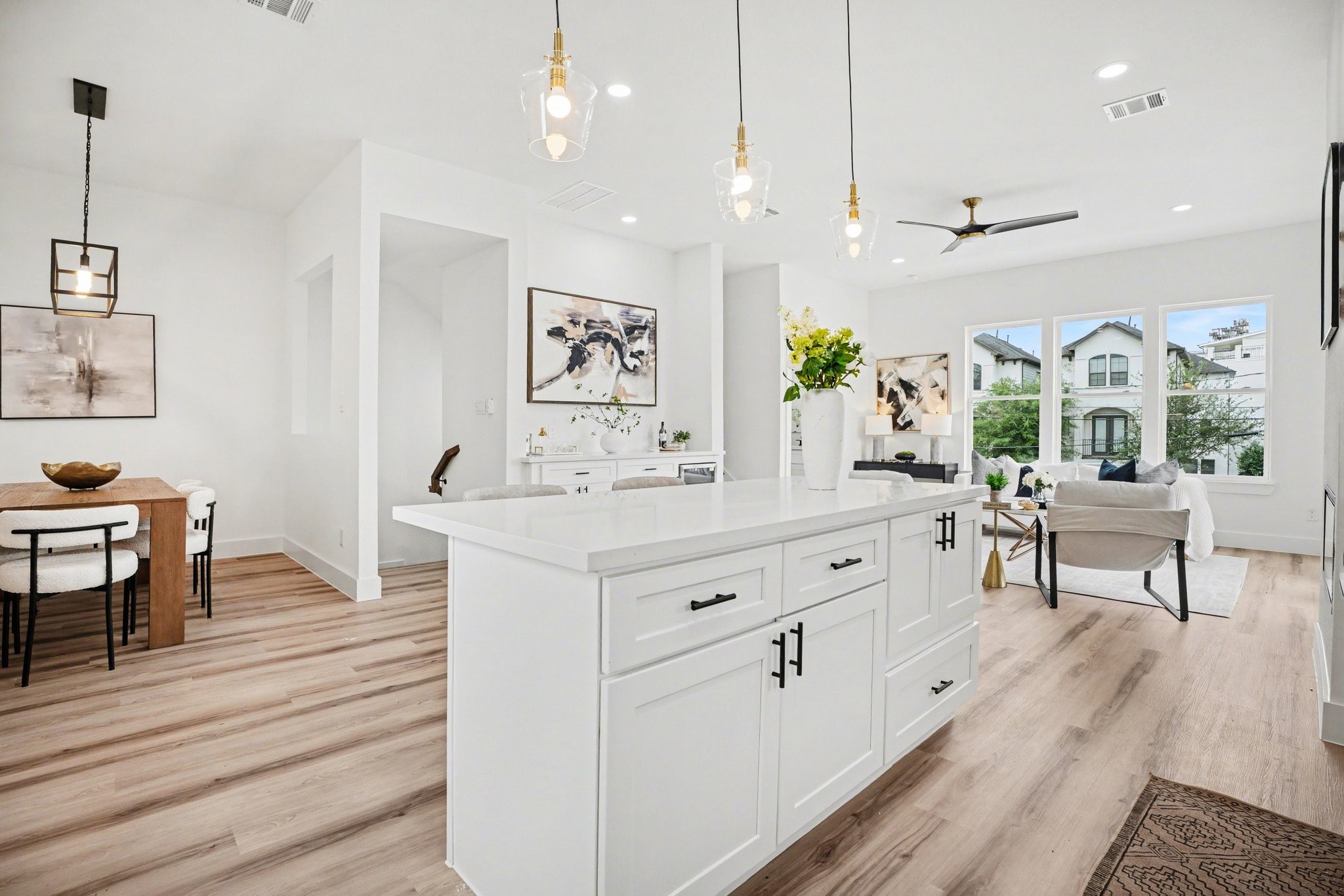 115 Milby Street Houston, TX 77003 - Photo 9 of 28 This photo showcases a modern, open-concept living space with a bright kitchen featuring a large island, contemporary light fixtures, and wood flooring. The adjacent dining area and cozy living room are well-lit by large windows, offering a welcoming and airy atmosphere.