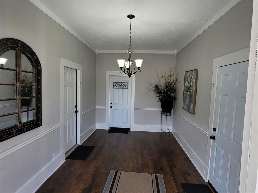 1103 East Moore Avenue, Unit 1 Terrell, TX 75160 - Photo 4 of 12 Entryway featuring crown molding, a notable chandelier, dark wood finished floors, and baseboards