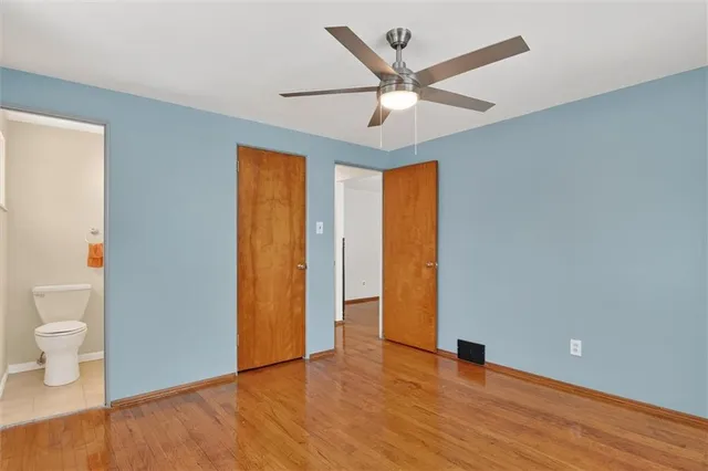 a view of an empty room with wooden floor and a ceiling fan