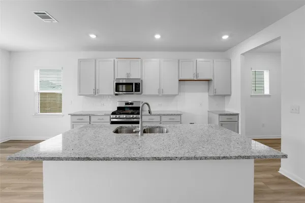 a kitchen with granite countertop a sink a stove a microwave a counter top space and cabinets