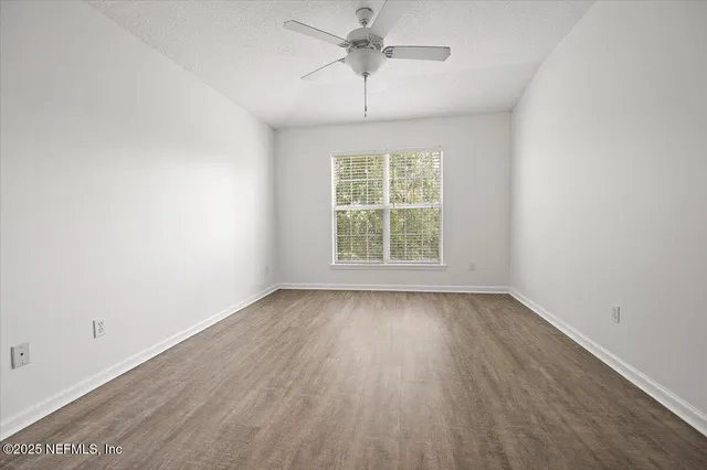 an empty room with wooden floor chandelier fan and windows