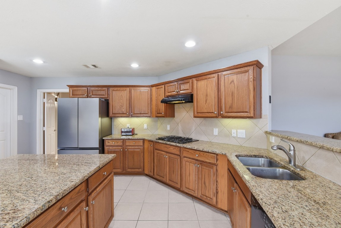 6534 Granbury Road Manvel, TX 77578 - Photo 25 of 49 a kitchen with stainless steel appliances granite countertop a sink and dishwasher refrigerator a sink with wooden cabinets