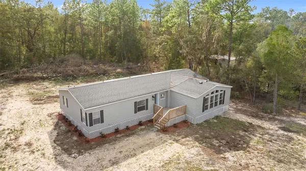 an aerial view of a house with yard and trees in the background