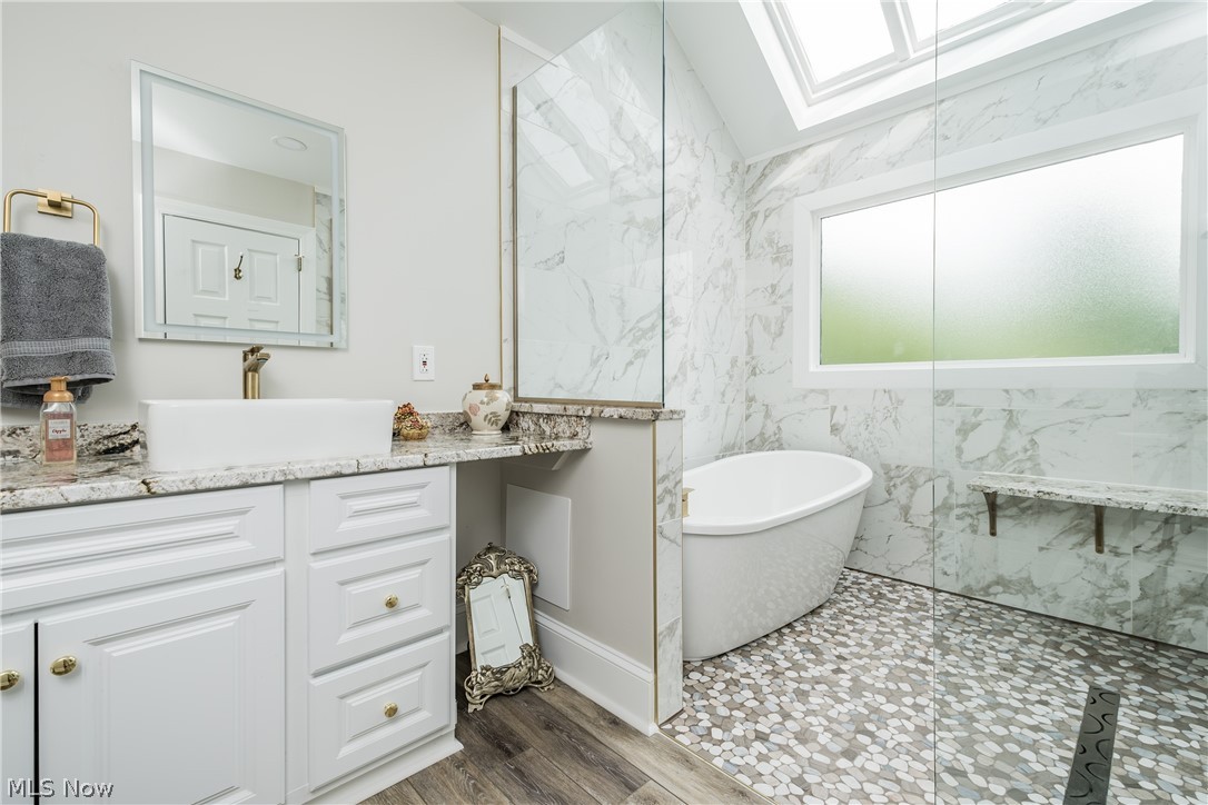 1415 Harbor Drive Northwest Canton, OH 44708 - Photo 30 of 46 Owners Bathroom featuring a freestanding soaking tub, walk in tile surround shower, hardwood / wood-style floors, tile walls, vaulted ceiling with skylight, and vanity
