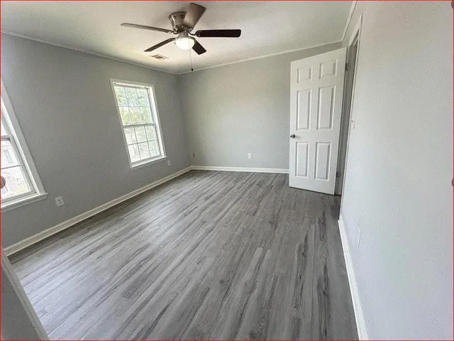 an empty room with wooden floor fan and windows