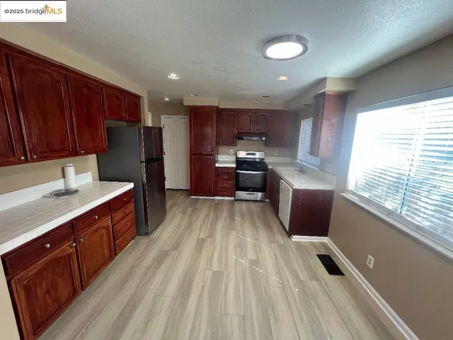 a kitchen with stainless steel appliances granite countertop a refrigerator a sink dishwasher a stove and white countertops with wooden floor