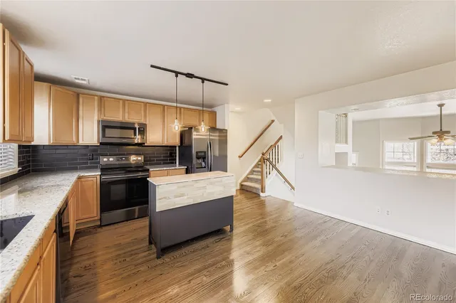 a kitchen with stainless steel appliances granite countertop a stove top oven a sink dishwasher a refrigerator and a dining table with wooden floor