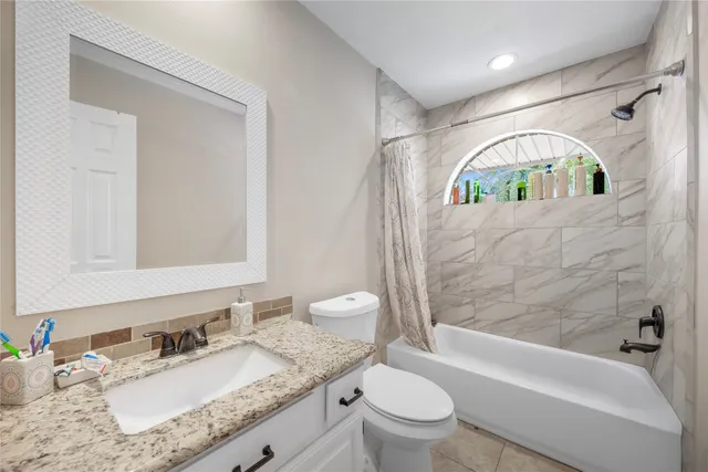 a bathroom with a granite countertop sink vanity mirror bathtub shower and a toilet