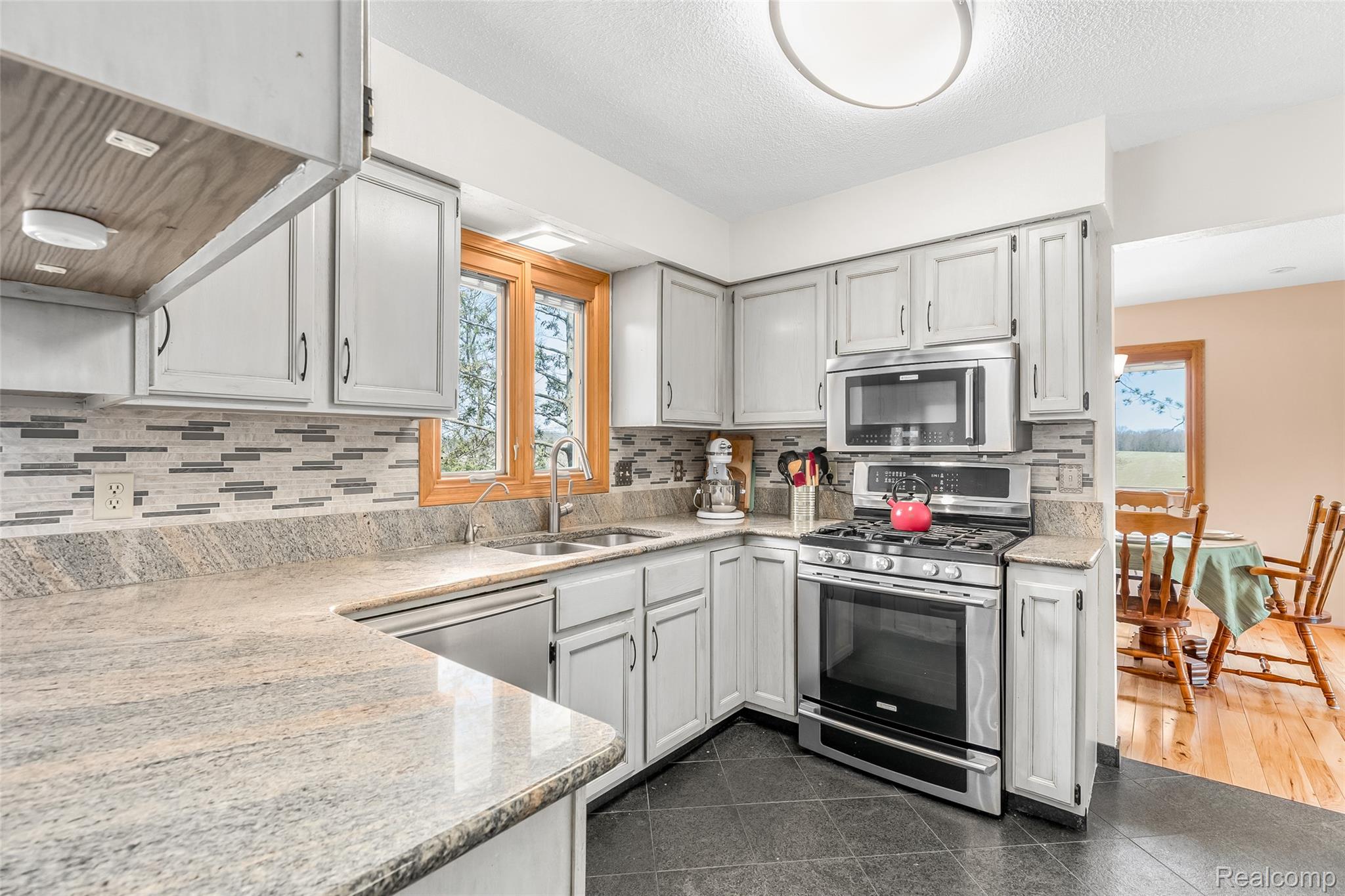15395 Osius Road Chelsea, MI 48118 - Photo 10 of 55 Kitchen featuring light gray cabinetry, stainless steel appliances, granite countertops, a tiled backsplash, and dark tile flooring