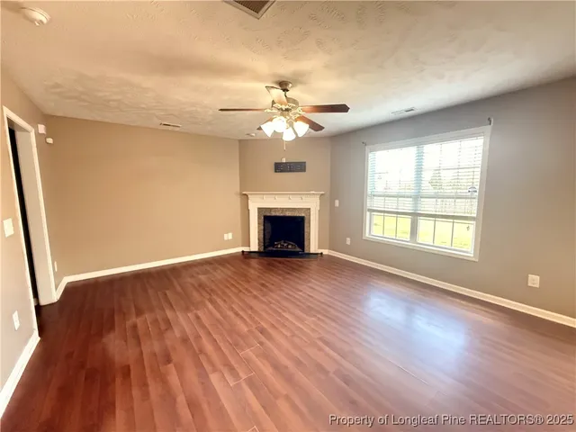 a view of an empty room with wooden floor fireplace and a window