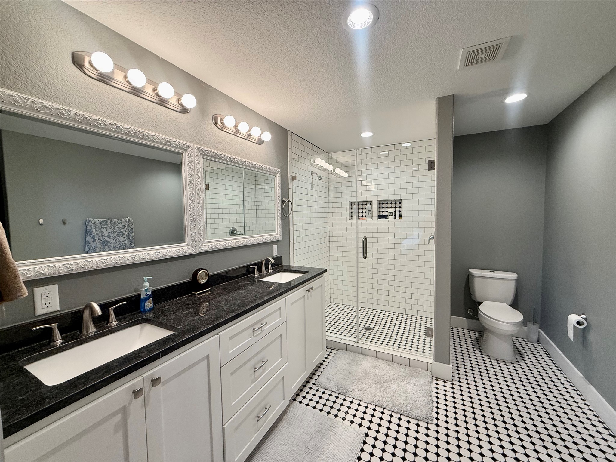 739 Pleasant Grove Road Elgin, TX 78621 - Photo 15 of 29 Bathroom featuring a double vanity with white cabinetry and dark countertops, individual framed mirrors, and a glass-enclosed shower with subway tile