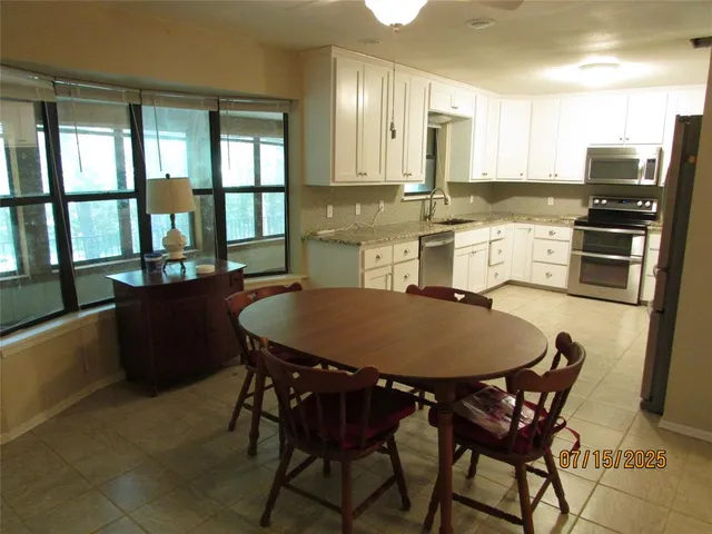 a kitchen with stainless steel appliances granite countertop a dining table chairs refrigerator and sink