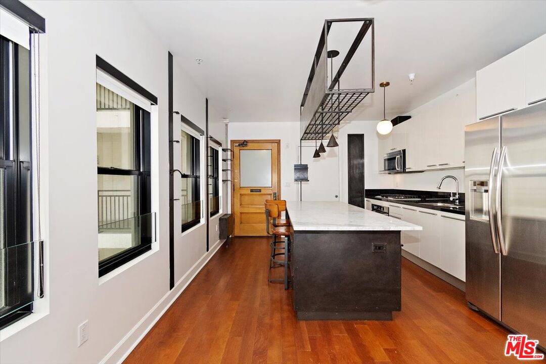 416 South Spring Street, Unit 609 Los Angeles, CA 90013 - Photo 5 of 24 a kitchen with stainless steel appliances a refrigerator a sink dishwasher a stove and white cabinets with wooden floor