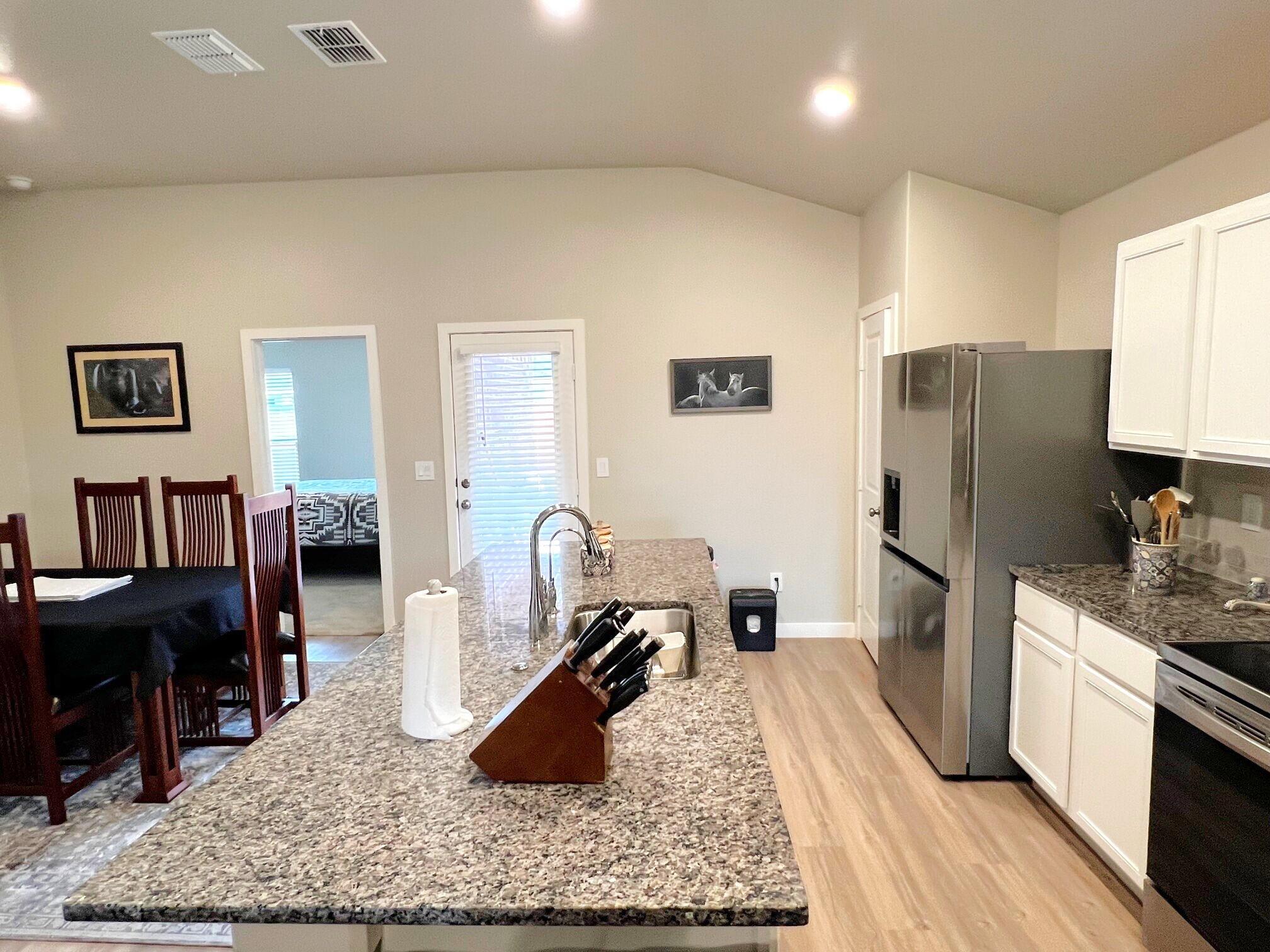2006 135th Street Lubbock, TX 79423 - Photo 8 of 24 a kitchen with stainless steel appliances granite countertop a refrigerator oven a sink a dining table and chairs with wooden floor