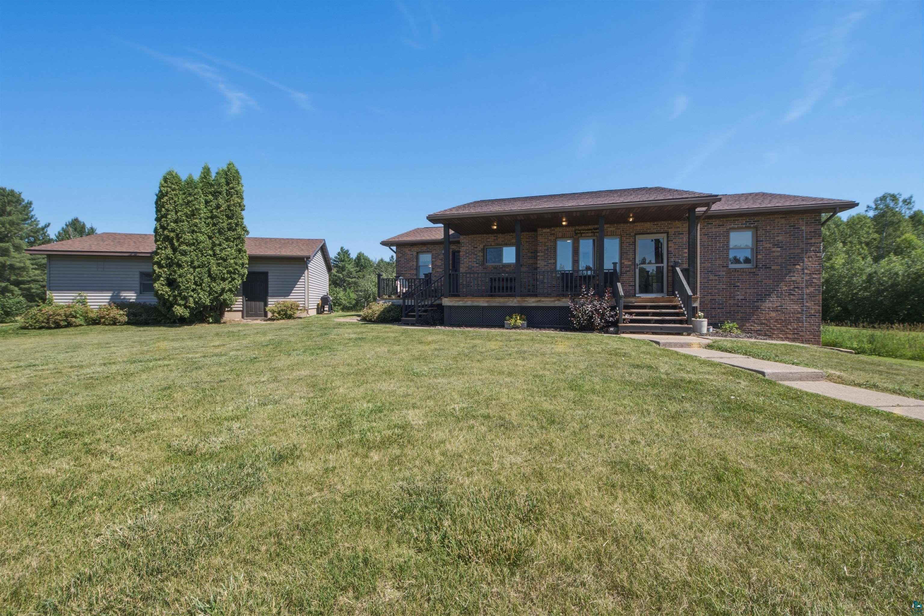 64260 Jolma Road Ashland, WI 54806 - Photo 27 of 35 Brick residence with a covered front porch featuring a dark railing, exterior lighting fixtures, and a multi-pane entry door