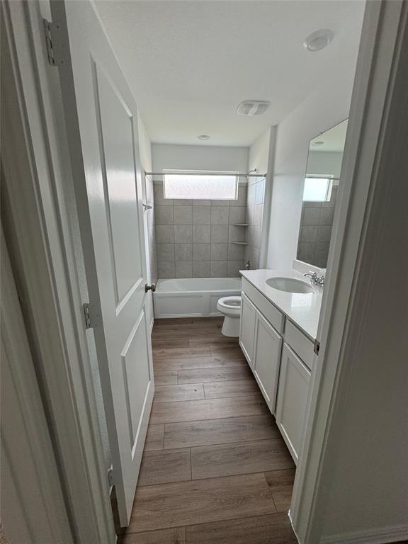 216 Jeffers Kyle, TX 78640 - Photo 9 of 19 Bathroom featuring a white vanity with an undermount sink and light-toned countertop, wood-finish flooring, a white bathtub, and light-toned tiled bath surround