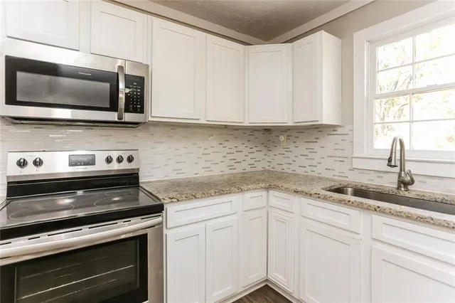 a kitchen with stainless steel appliances granite countertop white cabinets and a stove top oven