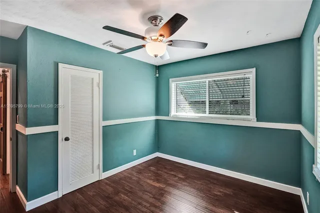an empty room with wooden floor fan and windows