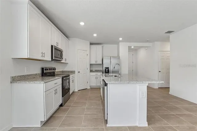 a kitchen with stainless steel appliances granite countertop a stove top oven a sink a refrigerator and white cabinets