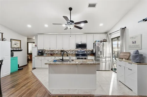 a kitchen with stainless steel appliances kitchen island granite countertop a stove top oven a refrigerator a sink and dishwasher with wooden floor