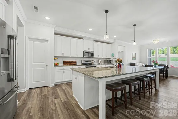 a kitchen with stainless steel appliances granite countertop a stove top oven a refrigerator a sink and chairs