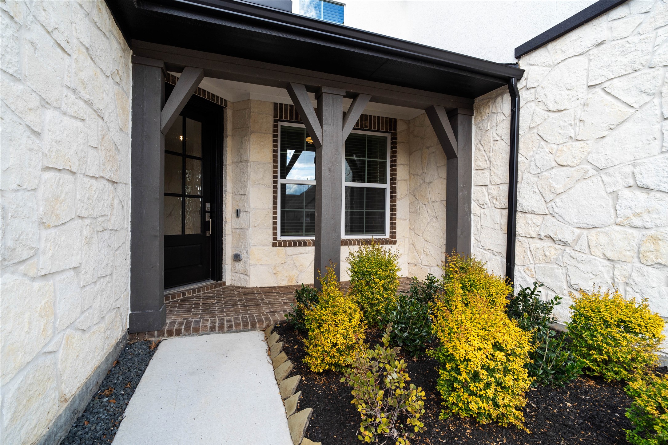 17315 July Moon Lane Conroe, TX 77302 - Photo 5 of 46 This covered front porch offers a grand first impression with its modern yet rustic aesthetic. The entrance features striking dark-stained timber beams and brackets that provide structural character against a beautiful white stone veneer façade.