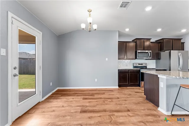 a kitchen with stainless steel appliances granite countertop a refrigerator a sink dishwasher a stove with wooden cabinets and floor