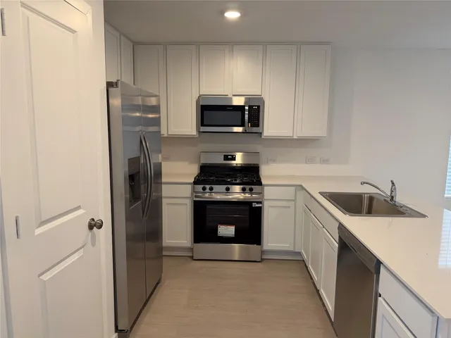 a kitchen with stainless steel appliances granite countertop a refrigerator a sink and white cabinets