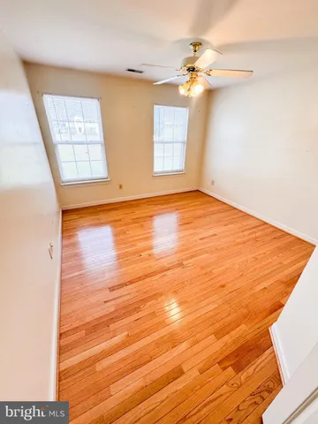 an empty room with wooden floor fan and windows