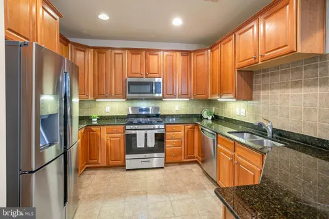 a kitchen with stainless steel appliances granite countertop a refrigerator a stove and a sink with wooden cabinets