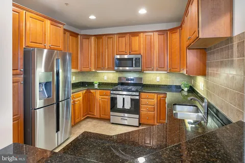 a kitchen with stainless steel appliances granite countertop a refrigerator a sink dishwasher a stove top oven a refrigerator and cabinets